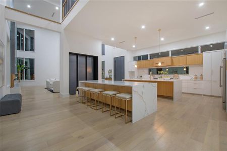 Kitchen with a spacious island, a towering ceiling, light stone counters, light hardwood / wood-style floors, and a kitchen bar