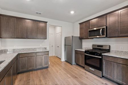 Kitchen featuring dark brown cabinets, light wood-type flooring, stainless steel appliances, and light stone counters