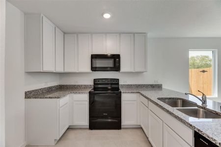 Kitchen with black appliances, white cabinets, sink, light tile patterned floors, and light stone countertops