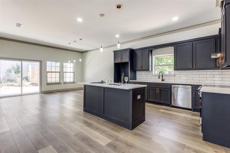 Kitchen featuring a center island with sink, pendant lighting, stainless steel dishwasher, and backsplash