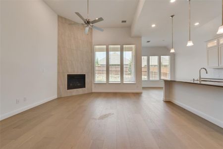 Unfurnished living room with wood-type flooring, a tiled fireplace, a wealth of natural light, and ceiling fan