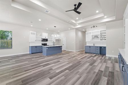 Kitchen featuring white cabinets, light hardwood / wood-style flooring, appliances with stainless steel finishes, blue cabinets, and a center island with sink