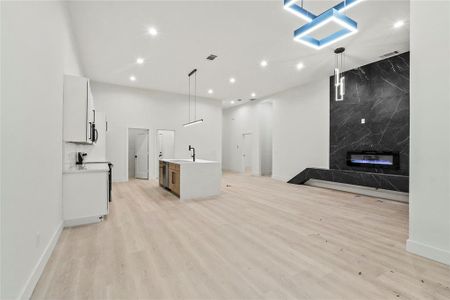 Kitchen featuring white cabinetry, light wood-type flooring, a kitchen island with sink, pendant lighting, and a high end fireplace