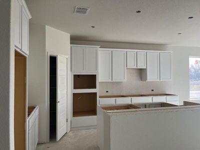 Kitchen featuring black electric stovetop, concrete floors, a kitchen island, visible vents, and white cabinetry