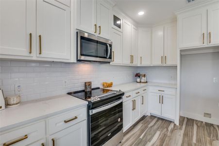 Kitchen featuring stainless steel appliances, light hardwood / wood-style floors, tasteful backsplash, light stone counters, and white cabinets