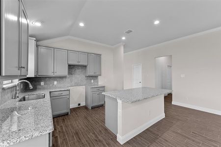 Kitchen featuring a kitchen island, sink, vaulted ceiling, gray cabinets, and light stone counters