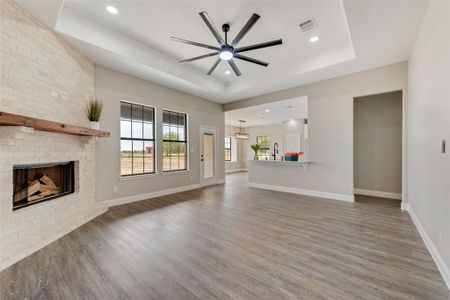 Unfurnished living room with ceiling fan, a raised ceiling, hardwood / wood-style flooring, and a brick fireplace