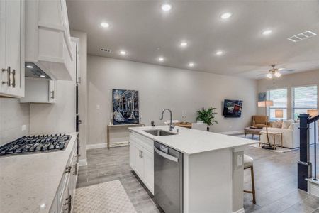 Kitchen featuring ceiling fan, stainless steel appliances, sink, white cabinets, and a kitchen island with sink