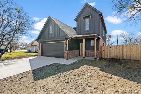 View of front of home with brick siding, roof with shingles, concrete driveway, board and batten siding, and fence