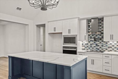 Kitchen with wall chimney exhaust hood, white cabinetry, light stone counters, a center island, and black appliances