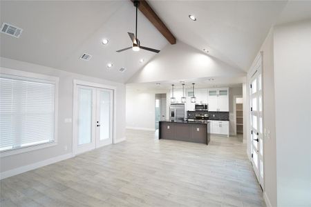 Kitchen with light hardwood / wood-style flooring, an island with sink, pendant lighting, white cabinets, and appliances with stainless steel finishes