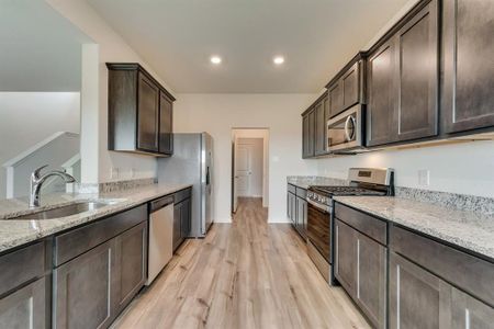 Kitchen with light hardwood / wood-style flooring, stainless steel appliances, sink, light stone counters, and dark brown cabinetry