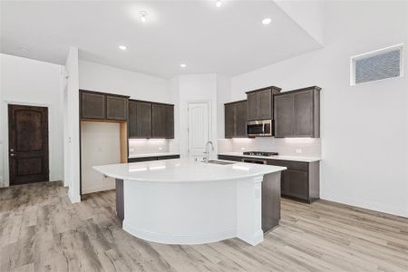 Kitchen featuring backsplash, sink, appliances with stainless steel finishes, light hardwood / wood-style flooring, and a center island with sink