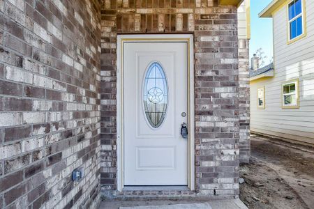 A new white front door with oval glass design on a brick house, unfinished landscaping, next to a house with yellow siding.