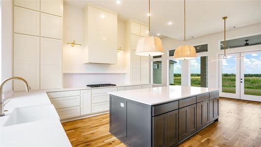 Kitchen with decorative light fixtures, light hardwood / wood-style floors, a kitchen island, white cabinetry, and sink