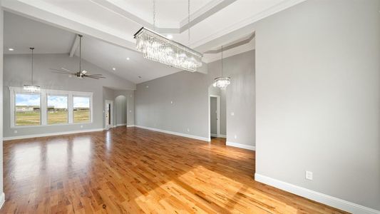 Unfurnished living room featuring arched walkways, high vaulted ceiling, light wood-style flooring, ceiling fan with notable chandelier, and baseboards