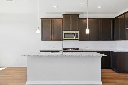 Kitchen featuring light hardwood / wood-style flooring, light stone counters, appliances with stainless steel finishes, and a kitchen island with sink