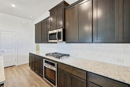 Kitchen featuring light stone countertops, light wood-type flooring, tasteful backsplash, dark brown cabinetry, and stainless steel appliances