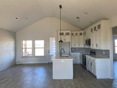 Kitchen featuring stainless steel appliances, sink, decorative light fixtures, dark hardwood / wood-style floors, and an island with sink