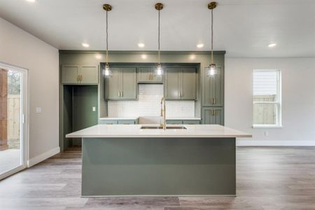 Kitchen featuring decorative backsplash, light hardwood / wood-style floors, an island with sink, decorative light fixtures, and sink