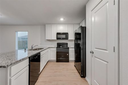 Kitchen with sink, light wood-type flooring, light stone counters, kitchen peninsula, and black appliances