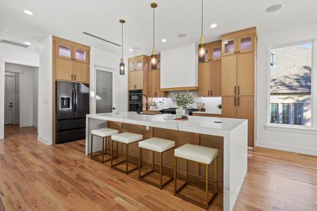 Kitchen with custom range hood, a spacious island, pendant lighting, light hardwood / wood-style flooring, and fridge with ice dispenser