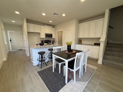 Kitchen featuring light tile patterned floors, stainless steel appliances, a kitchen island with sink, light stone countertops, and white cabinets