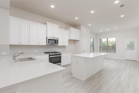 Kitchen featuring a kitchen island, sink, white cabinets, appliances with stainless steel finishes, and light hardwood / wood-style floors