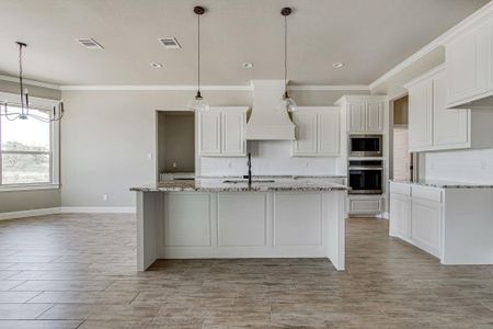 Kitchen featuring custom range hood, backsplash, appliances with stainless steel finishes, hanging light fixtures, and white cabinets