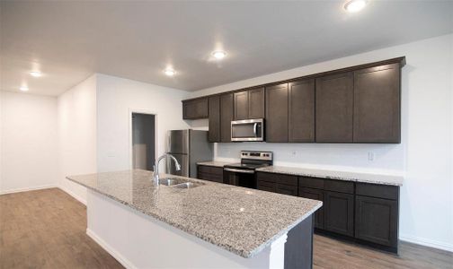 Kitchen featuring a center island with sink, sink, light wood-type flooring, appliances with stainless steel finishes, and light stone counters