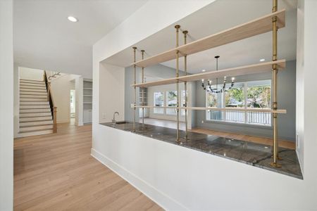 The entryway makes an impressive first statement with its open and airy design. Wide-plank light colored flooring flows seamlessly throughout, complemented by crisp white walls and natural light streaming in from oversized windows. A bold, custom shelving feature with brass accents and light wood shelves creates a stunning focal point while offering functional separation between spaces.