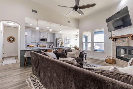 Living room featuring ornamental molding, light wood-type flooring, a tiled fireplace, and ceiling fan