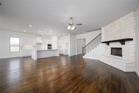 Unfurnished living room with ceiling fan, dark hardwood / wood-style floors, sink, and a stone fireplace