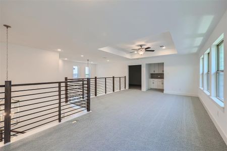 Carpeted empty room with ceiling fan with notable chandelier and a raised ceiling