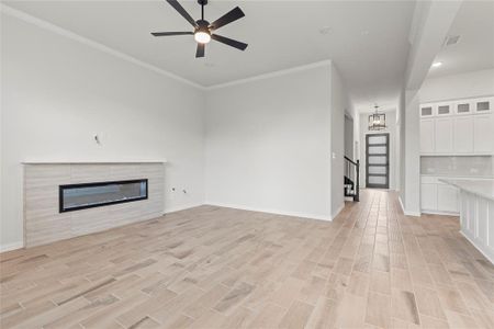 Unfurnished living room with ornamental molding, light hardwood / wood-style flooring, a fireplace, and ceiling fan with notable chandelier