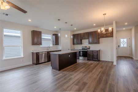 Kitchen featuring a kitchen island, ceiling fan with notable chandelier, pendant lighting, appliances with stainless steel finishes, and hardwood / wood-style flooring