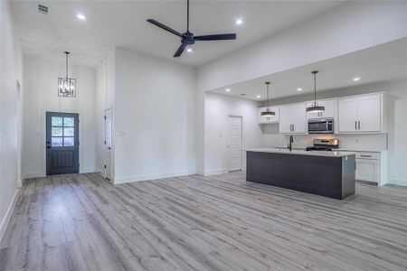 Kitchen with a high ceiling, stainless steel appliances, ceiling fan with notable chandelier, white cabinets, and light hardwood / wood-style floors