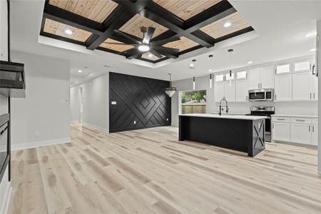 Kitchen with hanging light fixtures, an island with sink, light hardwood / wood-style floors, white cabinets, and appliances with stainless steel finishes