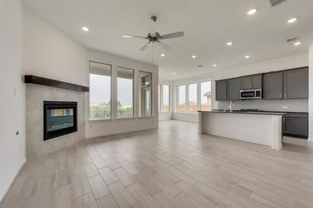 Kitchen featuring gray cabinetry, a center island with sink, ceiling fan, tasteful backsplash, and a tiled fireplace