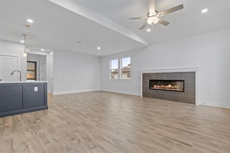 Unfurnished living room with ceiling fan, lofted ceiling, a fireplace, sink, and light hardwood / wood-style flooring