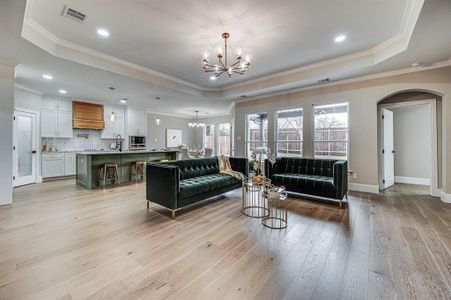 Living room featuring a raised ceiling, crown molding, a notable chandelier, and light wood-type flooring