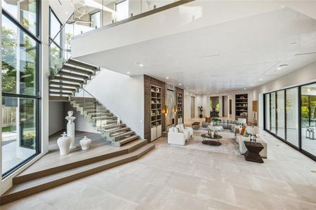 The foyer of this home is a masterpiece of modern design, featuring a two-story window that offers a breathtaking view of the front lawn and fills the space with natural light. The Harlem Caliza porcelain floor tile, Aria 6 Ring LED chandelier in polished brass, floating white oak and steel stairs with glass and steel railing, and inclination elevator all combine to create an elegant and functional entryway, enhanced by designer neutral wall paint and recessed LED lighting.