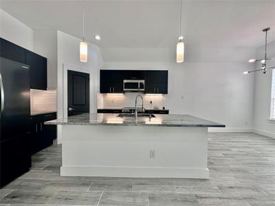 Kitchen with a center island with sink, decorative light fixtures, and stainless steel appliances