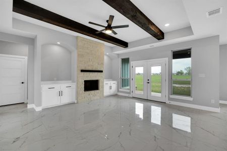 Unfurnished living room featuring light tile patterned floors, ceiling fan, french doors, a fireplace, and beamed ceiling