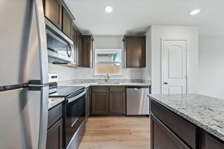 Kitchen with light stone countertops, sink, stainless steel appliances, light hardwood / wood-style floors, and dark brown cabinets