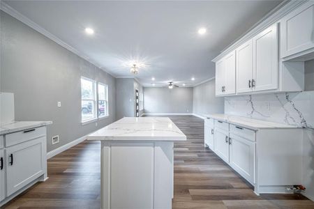 Kitchen with light stone countertops, a center island, white cabinetry, and dark hardwood / wood-style floors