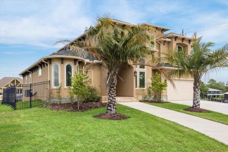 This is a modern two-story home featuring a stucco exterior with stone accents, a three-car garage, and a tile roof. Landscaping includes mature palm trees, and there's a welcoming arched entryway leading to a wood front door.