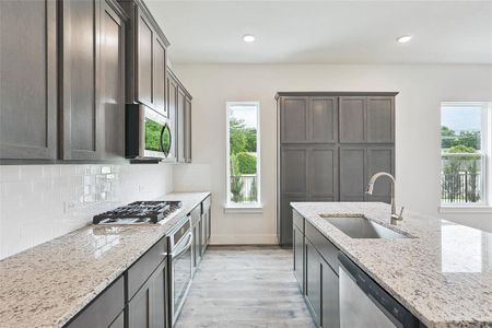 Kitchen with sink, appliances with stainless steel finishes, a wealth of natural light, light stone countertops, and backsplash