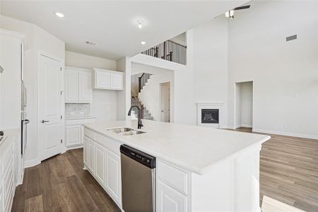 Kitchen with stainless steel dishwasher, sink, hardwood / wood-style floors, white cabinetry, and an island with sink