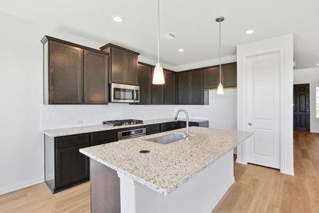 Kitchen with light stone countertops, stainless steel appliances, light hardwood / wood-style floors, sink, and a center island with sink